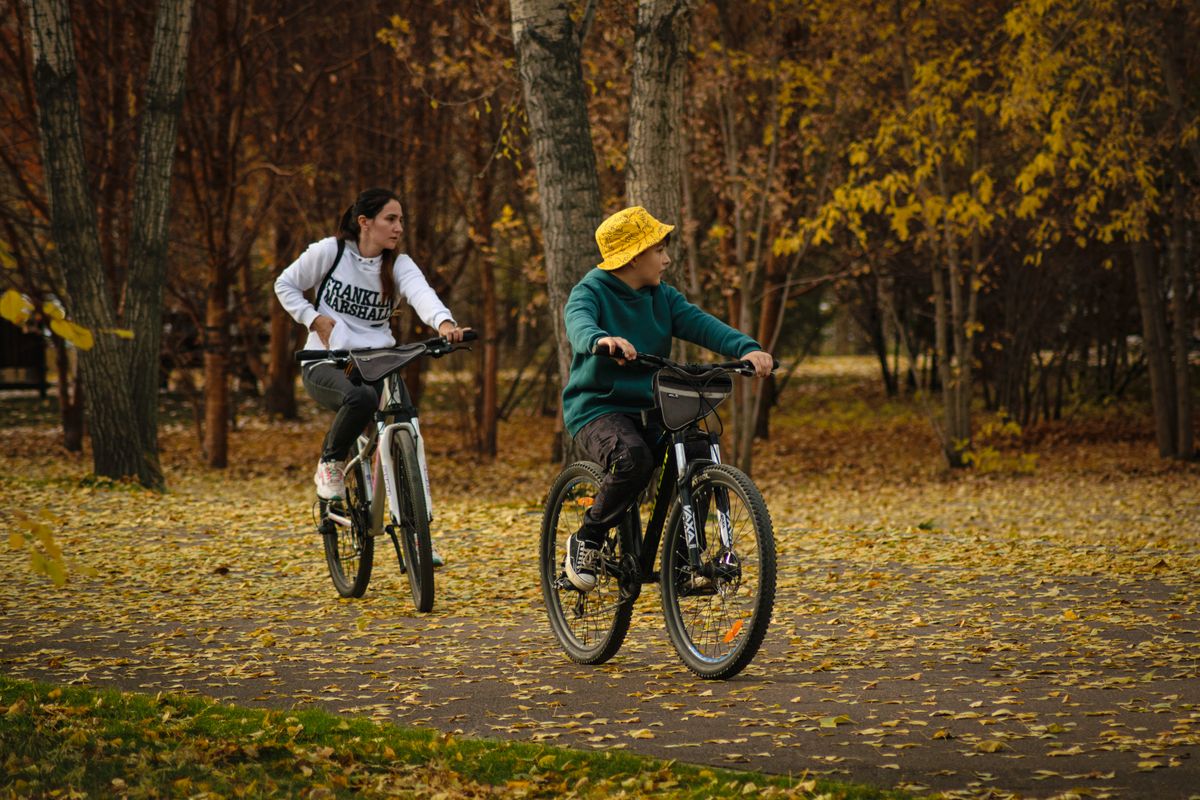 Mother and son riding bikes on a leafy park path in fall