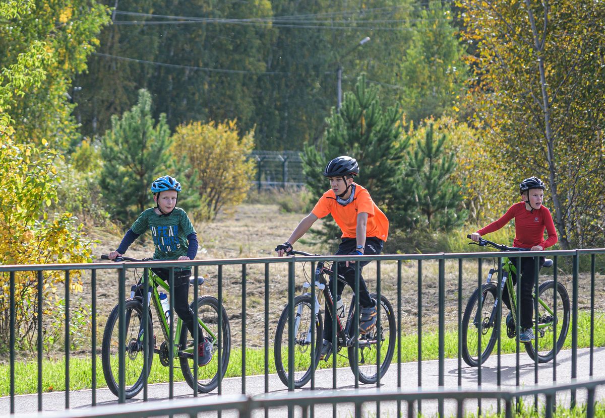 Three kids in helmets riding bikes along a park path