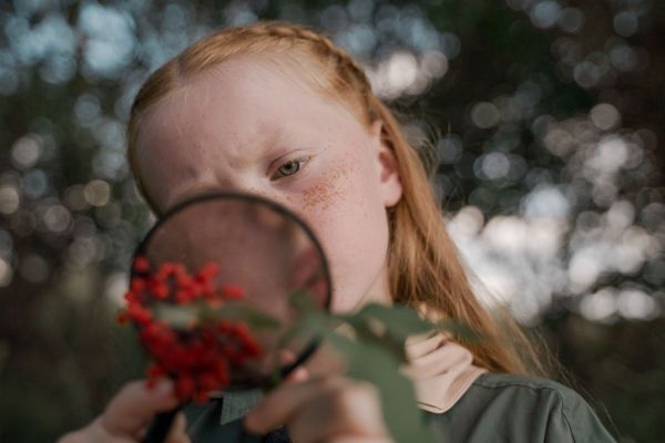 Girl looking at red berries through a magnifying glass