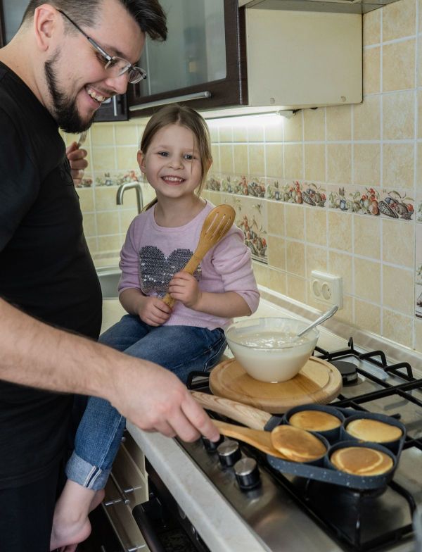 Smiling dad and daughter making pancakes together at the stove