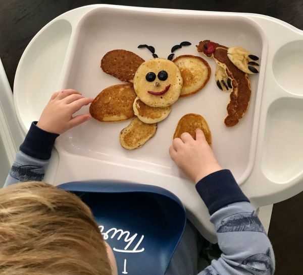 Little one making a butterfly out of pancakes with blueberry eyes