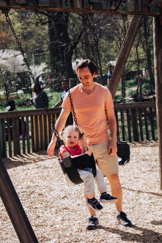 Dad pushing his little girl on a swing at a sunny park