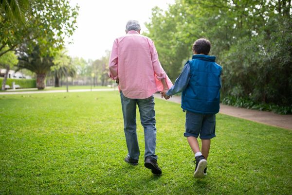 Grandpa and grandson walking hand in hand through a green park
